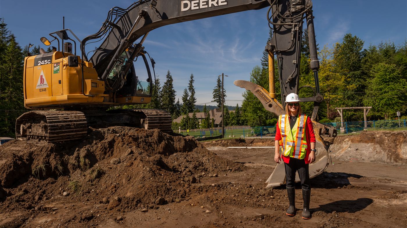 Juli Halliwell-Ferrero on site during excavation for the Anmore Community Hub, with heavy equipment at work behind her