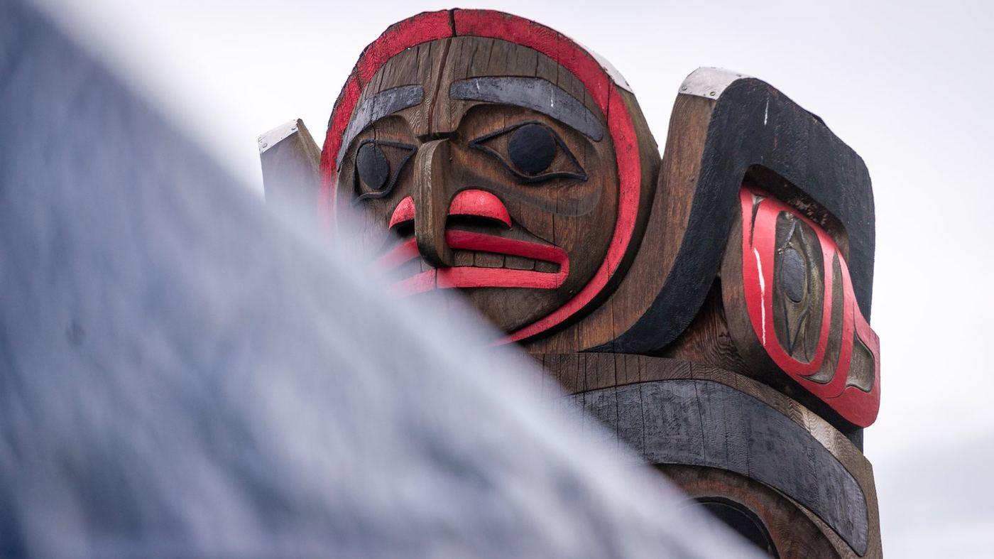 Detail of a carved and painted house pole standing against an overcast sky