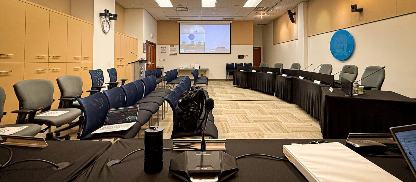 An empty Council chamber set up before a meeting, with microphones, name cards and the presentation screen ready
