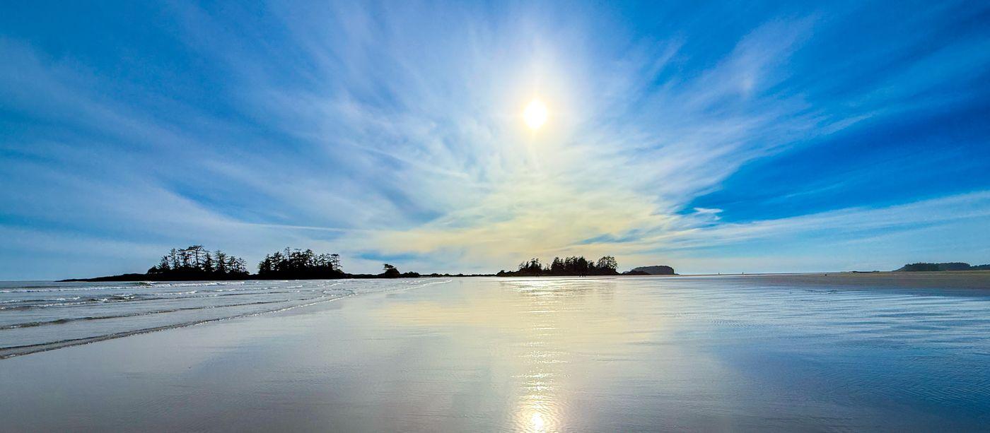 A wide, open beach at low tide with islands on the horizon and sun on the wet sand